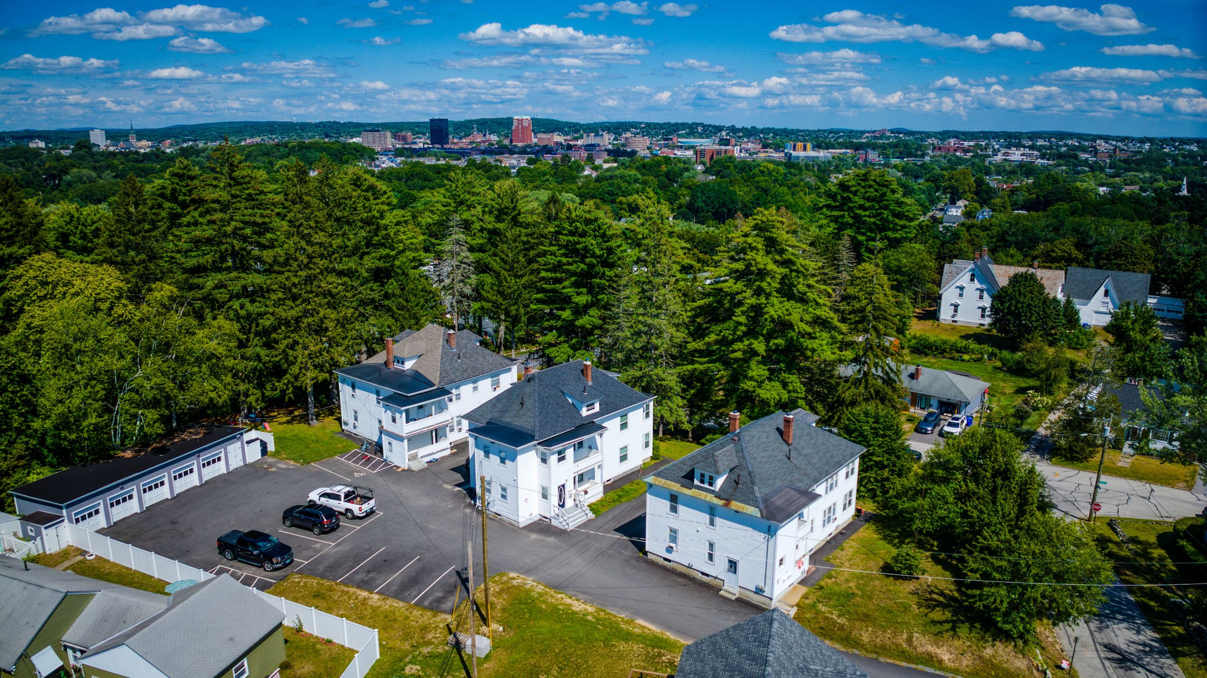 Aerial view of three white houses on a wooded hill, with downtown Manchester behind them